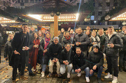 Auf dem Bild sieht man eine Gruppe Studierender, die zusammen an einem Stand auf dem Weihnachtsmarkt stehen.