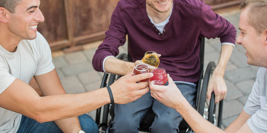 Menschen im Rollstuhl stoßen mit Getränken an