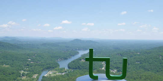 TU Logo auf einem Fernglas mit Blick zu einer Flusslandschaft