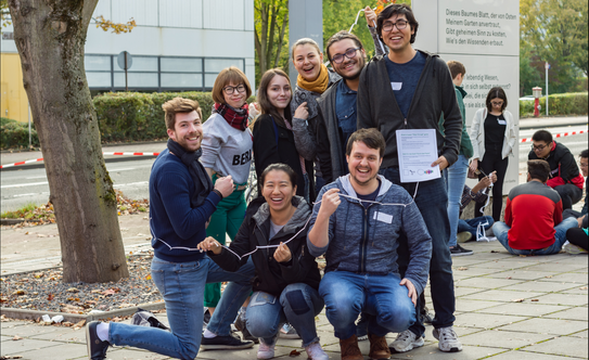Come2Campus a group of international students in front of the International Meeting Center of the TU Dortmund University playing a game; in the background another group