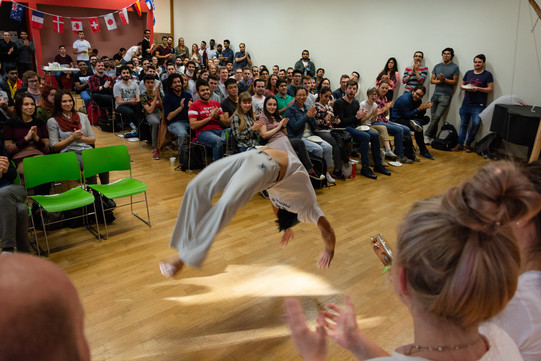 Come2Campus Im Vordergrund ein Capoeira Tänzer, im Hintergrund viele internationale Studierende, die zuschauen und applaudieren