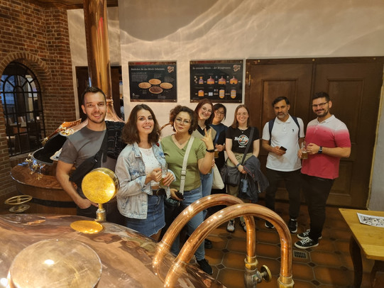 Menschen stehen vor den Kupferkesseln einer Brauerei.