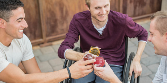 Behinderung oder chronische Erkrankung Menschen im Rollstuhl stoßen mit Getränken an