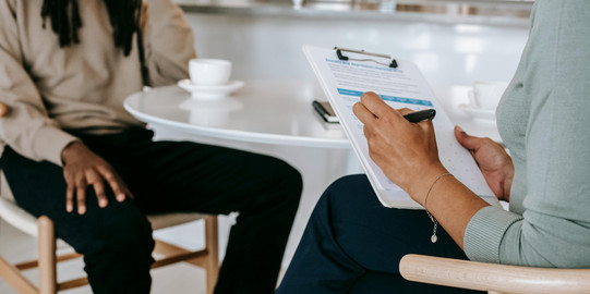 Two people at a table; study advisor holding a clipboard