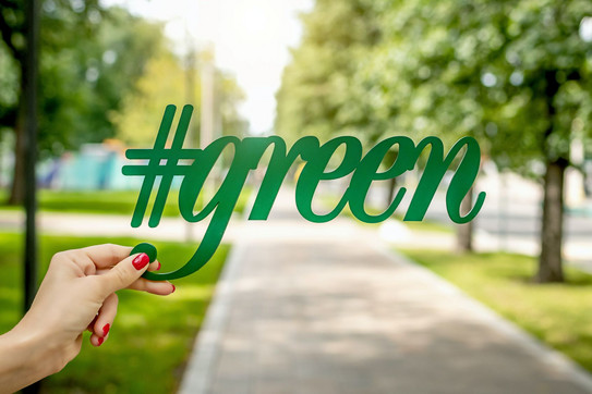 artem-beliaikin-BpQ-ClsKeXg-unsplash.jpg eine Person hält den Schriftzug "#green", mit einem Park im Hintergrund an einem sonnigen Tag