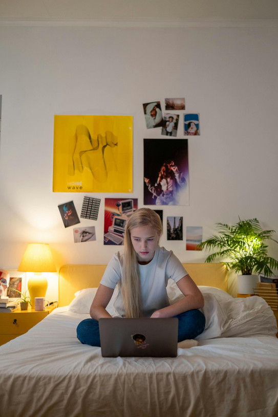 Eine Studierende sitzt auf einem Bett und blickt konzentriert auf den Laptop vor ihr