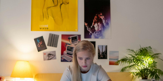 Eine Studierende sitzt auf einem Bett und blickt konzentriert auf den Laptop vor ihr