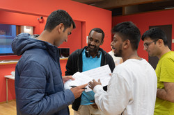 Sprachcafé_9 A group of international students are standing together and talking. They show each other something on pieces of paper.