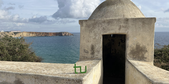 Portugal Das TU-Logo steht neben einem kleinen Turm an einem Küstenabschnitt