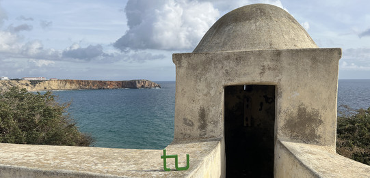 Portugal Das TU-Logo steht neben einem kleinen Turm an einem Küstenabschnitt