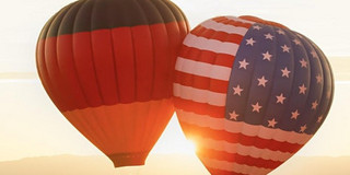 E_112021_Hasso-Plattner_cdn.evbuc.com_images_166610739.jpg 2 Heißluftballons, eins mit der deutschen Flagge und ein mit der US-Flagge, schweben in der Luft