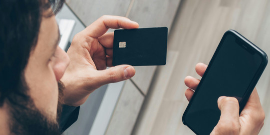 Ein Mann der eine Bankkarte und ein Handy in den Händen hält
