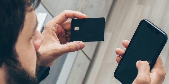 Ein Mann der eine Bankkarte und ein Handy in den Händen hält