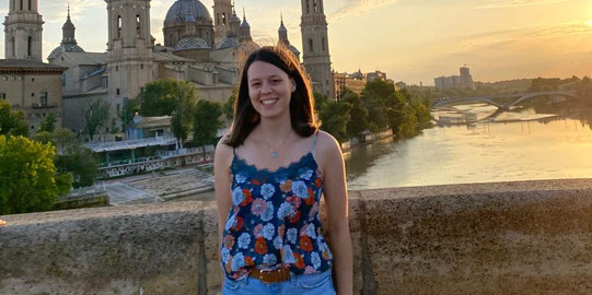 Profilbild Here you can see the student standing on a bridge over a river in summer with a castle in the background.
