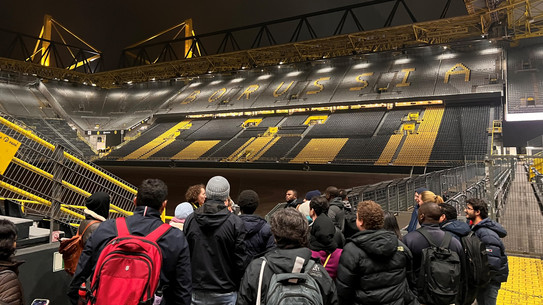 Menschen schauen von der Tribüne in ein Fußballstadion.
